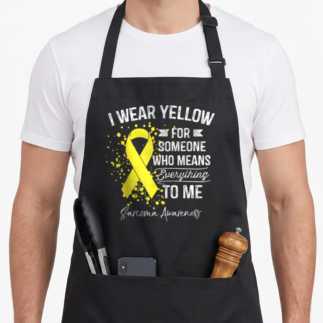 Sarcoma ribbon apron - Yellow ribbon with white text I wear yellow for someone who means everything to me Sarcoma — shown on a black cotton canvas apron against a white background