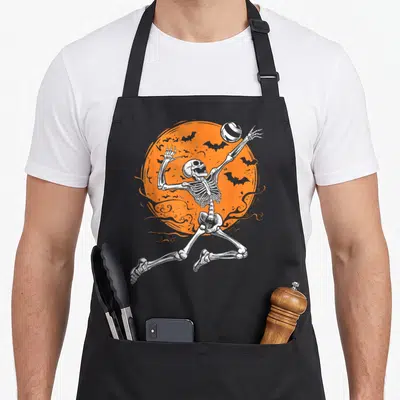 Volleyball skeleton halloween apron - White skeleton jumping to spike volleyball in front of orange moon with bats — shown on a black cotton canvas apron against a white background