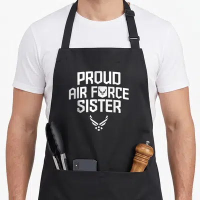 Proud air military apron - White PROUD AIR FORCE SISTER text with shield and winged emblem below — shown on a black cotton canvas apron against a white background