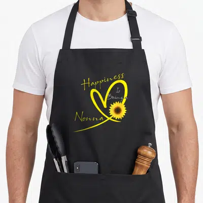 Nonna sunflower apron - Happiness Is Being a Nonna text with yellow heart and sunflower — shown on a black cotton canvas apron against a white background