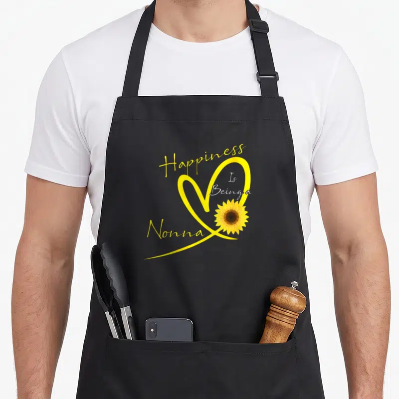 Nonna sunflower apron - Happiness Is Being a Nonna text with yellow heart and sunflower — shown on a black cotton canvas apron against a white background
