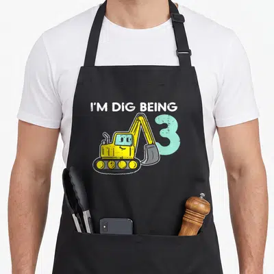 Dig birthday apron - Yellow cartoon excavator overlapping a light blue number 3 under arched white text reading I'M DIG — shown on a black cotton canvas apron against a white background
