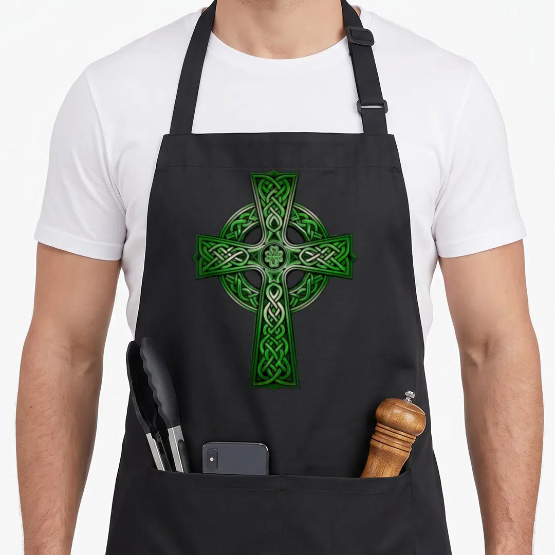 Irish cross apron - Green and silver Celtic cross with intricate knotwork filling the center design — shown on a black cotton canvas apron against a white background