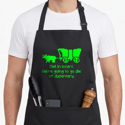 Die get loser apron - Lime green ox pulling covered wagon with sarcastic text about dysentery — shown on a black cotton canvas apron against a white background
