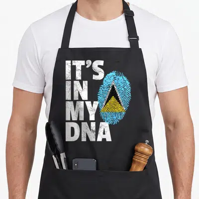 Saint country apron - IT'S IN MY DNA text beside Saint Lucia flag fingerprint in blue yellow black white — shown on a black cotton canvas apron against a white background