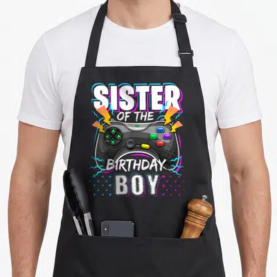 Sister birthday video game apron - Cartoon game controller with lightning bolts and sister of the birthday boy text — shown on a black cotton canvas apron against a white background