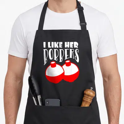 Bobber couple apron - I LIKE HER BOBBERS text above two red and white cartoon fishing floats — shown on a black cotton canvas apron against a white background