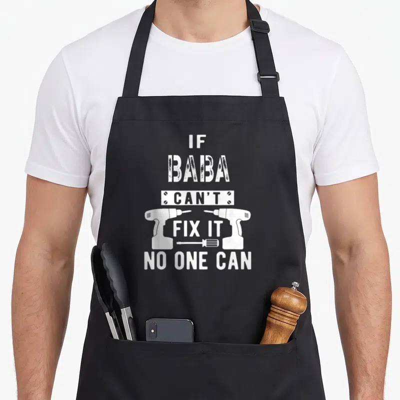 Baba grandpa apron - White distressed text IF BABA CAN'T FIX IT flanked by two drills with a screwdriver below — shown on a black cotton canvas apron against a white background
