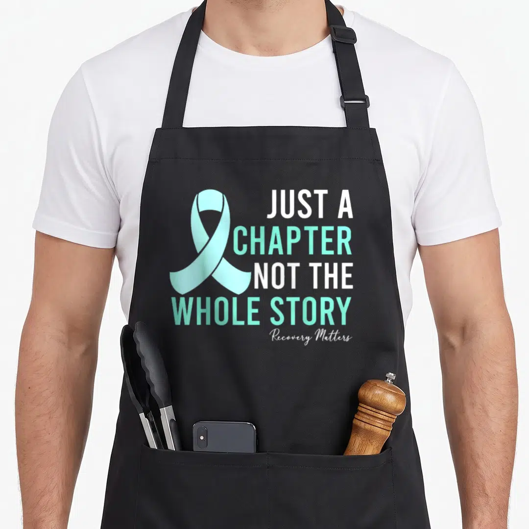 Important addiction recovery apron - Mint green awareness ribbon next to stacked white and mint text reading Just — shown on a black cotton canvas apron against a white background