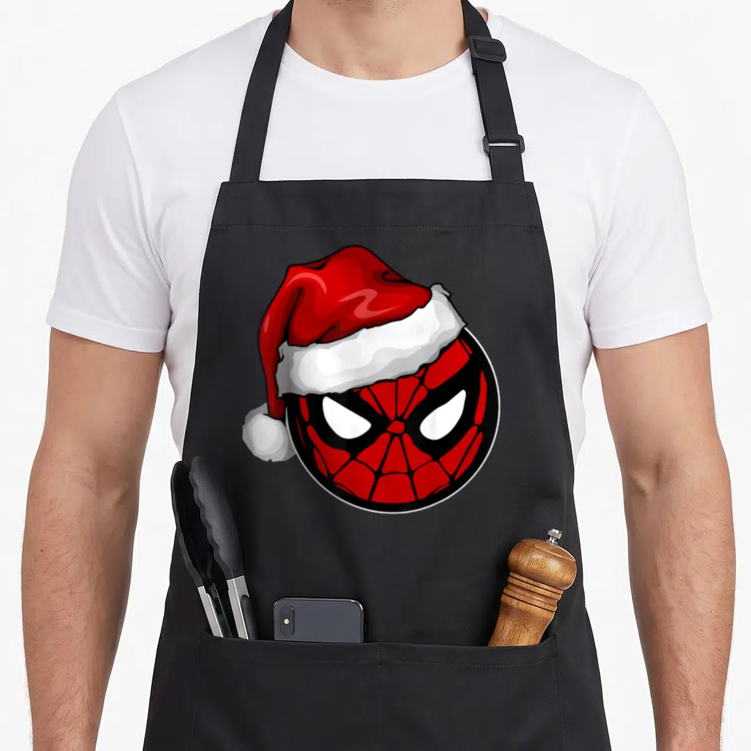 Hat santa aprons - Cartoon Spider-Man head wearing a red Santa hat with white trim and pom-pom — shown on a black cotton canvas apron against a white background
