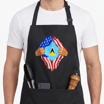 Lucian blood apron - Two brown hands tear a USA flag revealing a Saint Lucia flag with blue background and triangle — shown on a black cotton canvas apron against a white background
