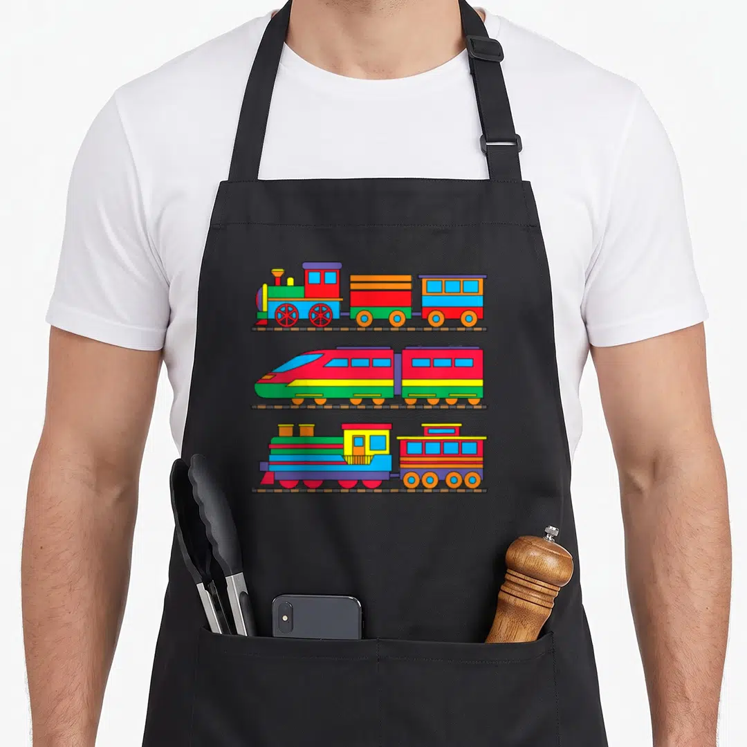 Railway steam locomotive apron - Three colorful cartoon trains stacked vertically on brown tracks in red, blue, yellow — shown on a black cotton canvas apron against a white background