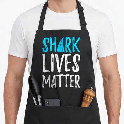 Shark week apron - Stacked blue and white text reading SHARK LIVES MATTER with a fin replacing — shown on a black cotton canvas apron against a white background