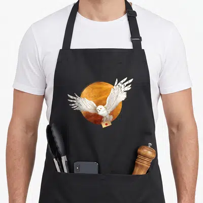 Hedwig potter apron - Realistic white owl flying before orange circle carrying tan envelope in talons — shown on a black cotton canvas apron against a white background