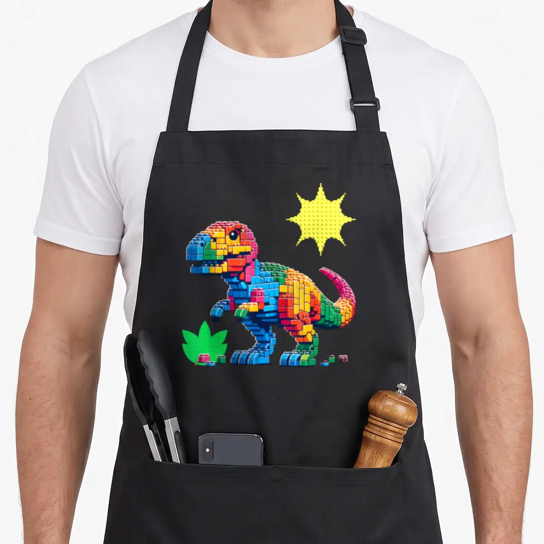 Brick building apron - Pixel dinosaur built from red blue yellow green bricks with sun and loose pieces at base — shown on a black cotton canvas apron against a white background