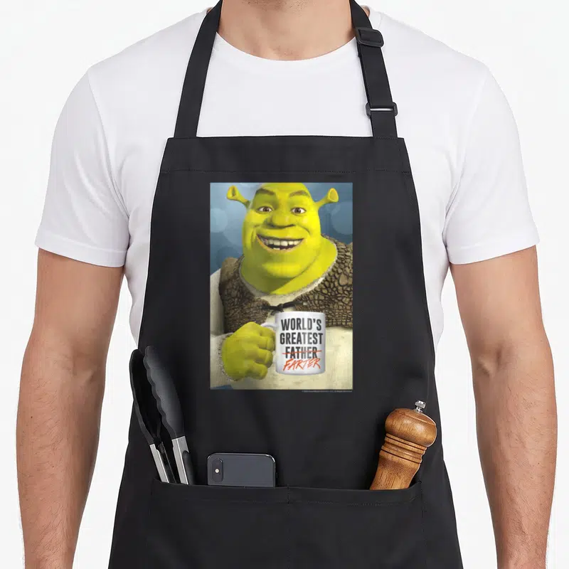 Father worlds greatest dad apron - Shrek holds white mug with WORLD'S GREATEST FATHER crossed out in red and FARTER — shown on a black cotton canvas apron against a white background