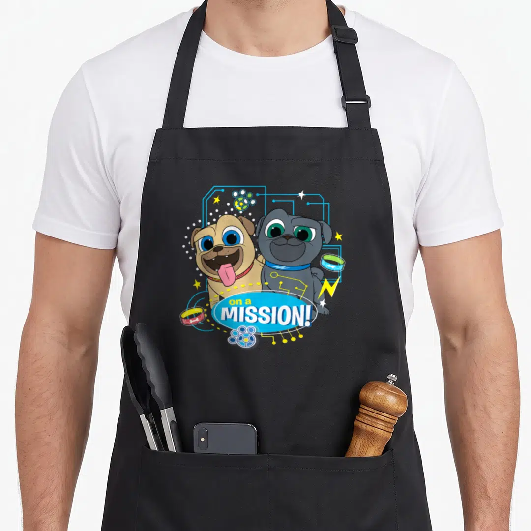 Mission dog apron - Two cartoon puppies with circuit lines and blue oval text on a mission — shown on a black cotton canvas apron against a white background