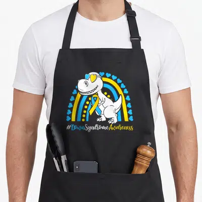 Extra dinosaur apron - White T-rex with heart sunglasses and blue yellow ribbon under #DownSyndromeAwareness text — shown on a black cotton canvas apron against a white background