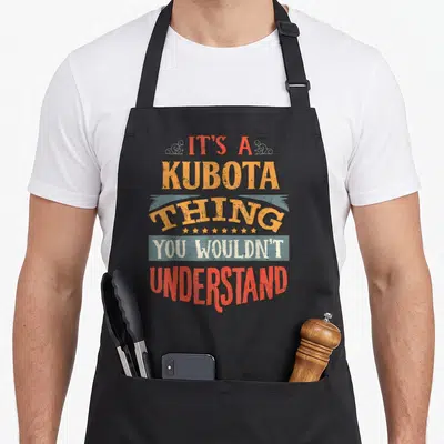 Funny tailor apron - Stacked retro text reading It's a Kubota Thing You Wouldn't Understand in red yellow and blue grey — shown on a black cotton canvas apron against a white background