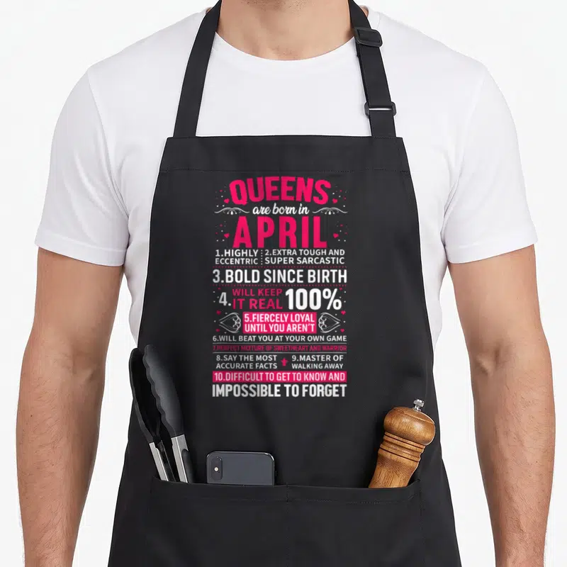 Cute queen april apron - Pink and white typography listing ten sass traits for April queens including sarcasm — shown on a black cotton canvas apron against a white background