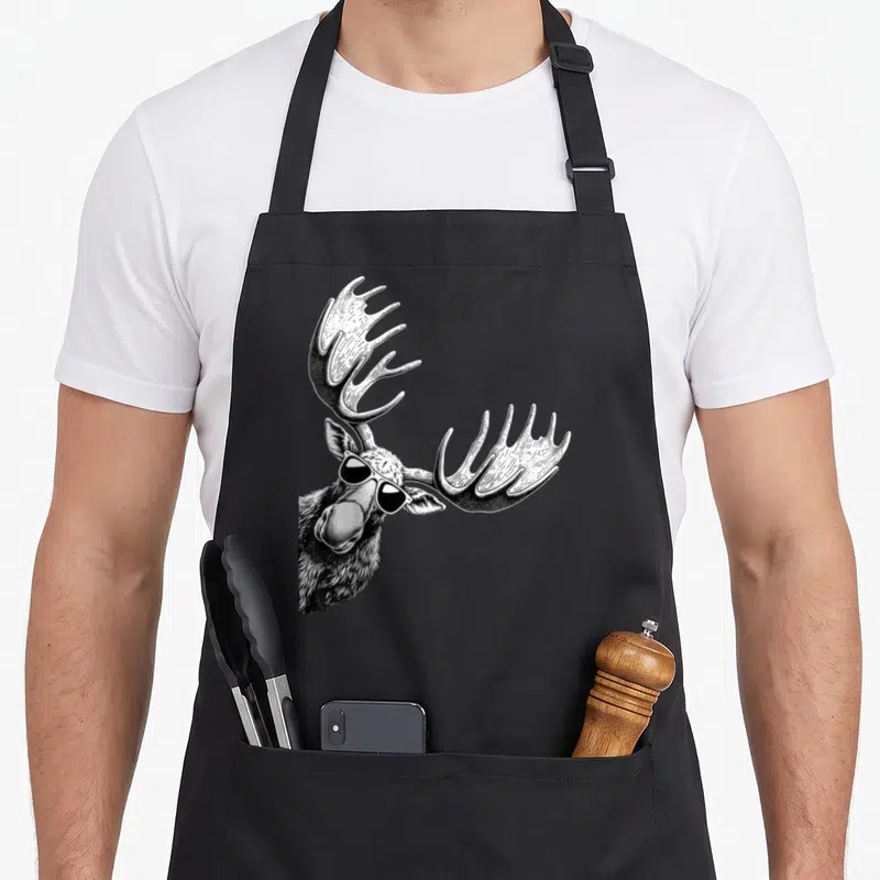 Sunglass moose apron - Realistic black and white moose head wearing sunglasses with stippled antlers — shown on a black cotton canvas apron against a white background