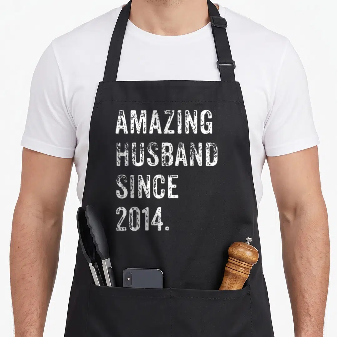 Amazing husband wedding aprons - White distressed text AMAZING HUSBAND SINCE 2014 stacked on black background — shown on a black cotton canvas apron against a white background