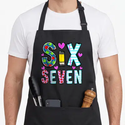 Six seven teacher apron - Cartoon text SIX SEVEN with pencil I, apple patterns, and pink hearts in blue pink yellow red — shown on a black cotton canvas apron against a white background