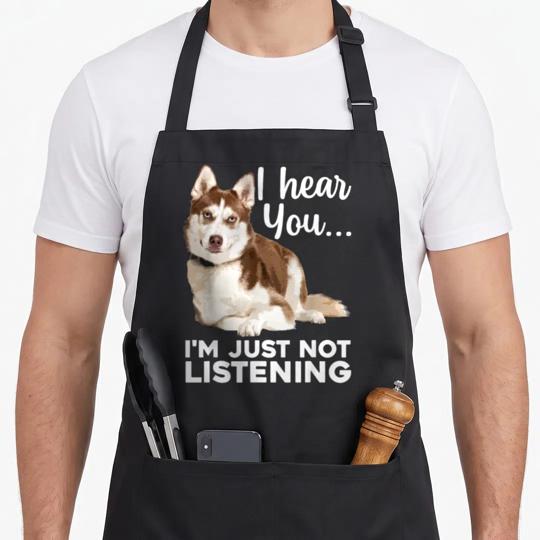 Dog siberian husky apron - Cartoon brown and white husky lying down with text I hear You I'm Just Not Listening — shown on a black cotton canvas apron against a white background