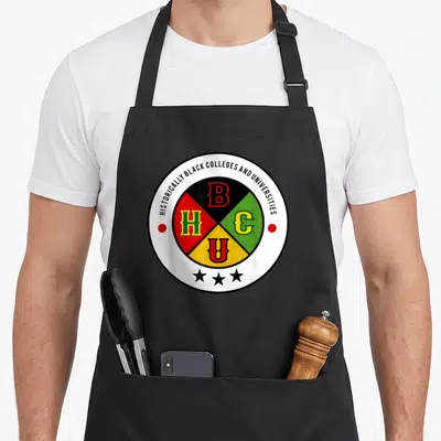 Grad african american aprons - Circular HBCU emblem with four colored quadrants containing letters B H C U and three — shown on a black cotton canvas apron against a white background