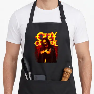 Memoir ozzy osbourne apron - Ozzy Osbourne graphic with yellow text and red splatter background — shown on a black cotton canvas apron against a white background