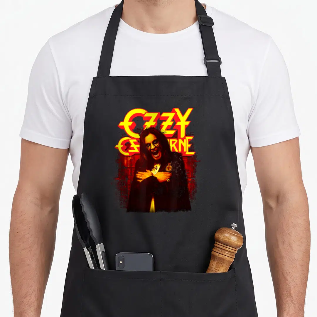 Memoir ozzy osbourne apron - Ozzy Osbourne graphic with yellow text and red splatter background — shown on a black cotton canvas apron against a white background