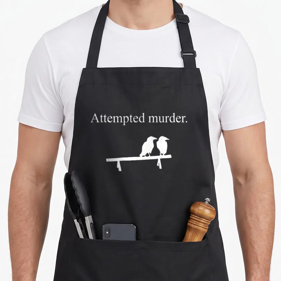 Attempted crow mom apron - White text attempted murder above two white crows sitting on a bench — shown on a black cotton canvas apron against a white background