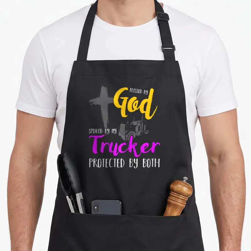 Pampered blessed god apron - Grey cross and truck graphic with stacked yellow magenta white text reading Blessed by God — shown on a black cotton canvas apron against a white background