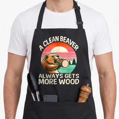 Clean beaver apron - Retro sunset circle with brown beaver chewing log and cream text A Clean Beaver Always Gets More — shown on a black cotton canvas apron against a white background