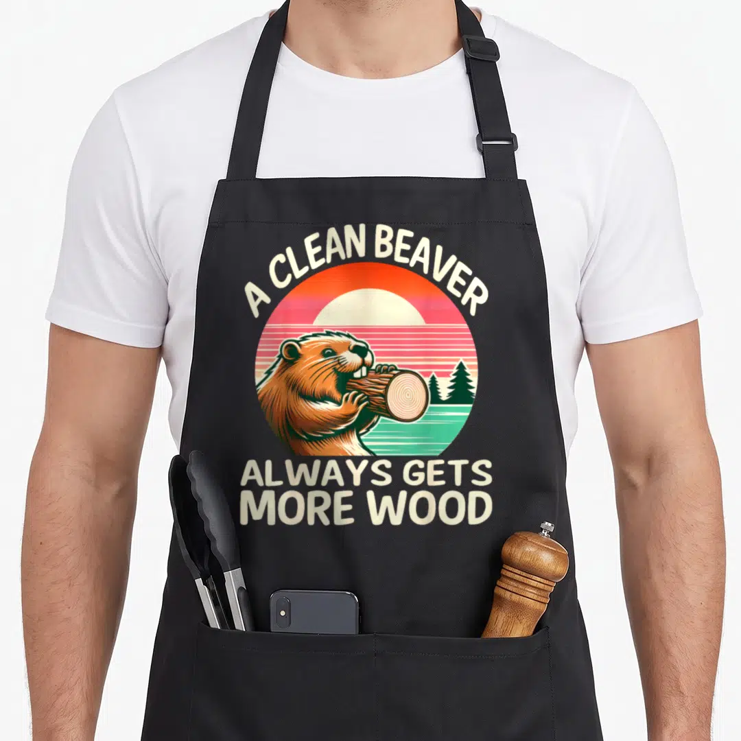 Clean beaver apron - Retro sunset circle with brown beaver chewing log and cream text A Clean Beaver Always Gets More — shown on a black cotton canvas apron against a white background