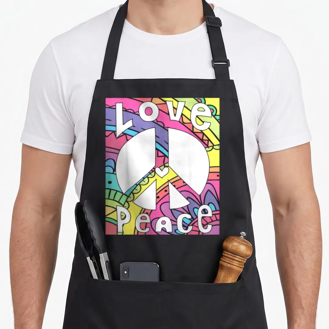 Sign 60s hippie apron - White peace sign with small heart center surrounded by colorful psychedelic patterns and love — shown on a black cotton canvas apron against a white background