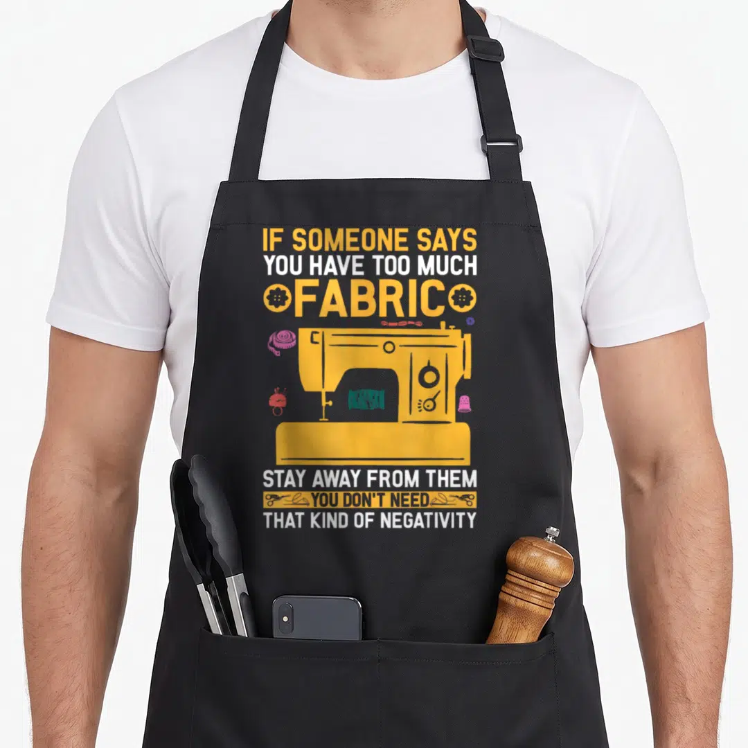 Sewer quilting apron - Yellow sewing machine with fabric advice quote and scattered notions in teal and pink — shown on a black cotton canvas apron against a white background
