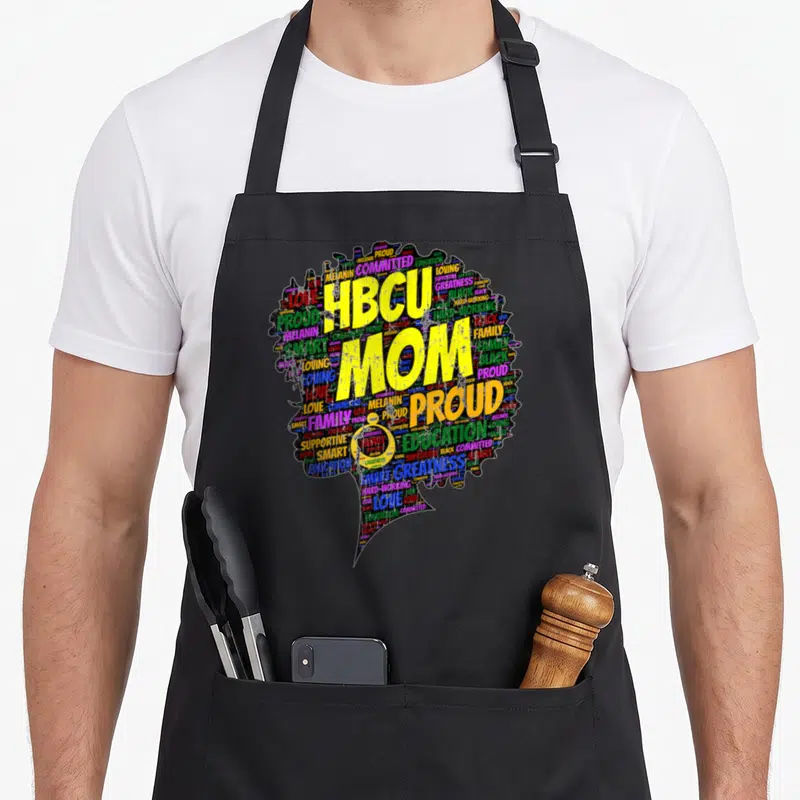 Hbcu graduation apron - HBCU MOM PROUD yellow text over colorful word cloud woman silhouette — shown on a black cotton canvas apron against a white background