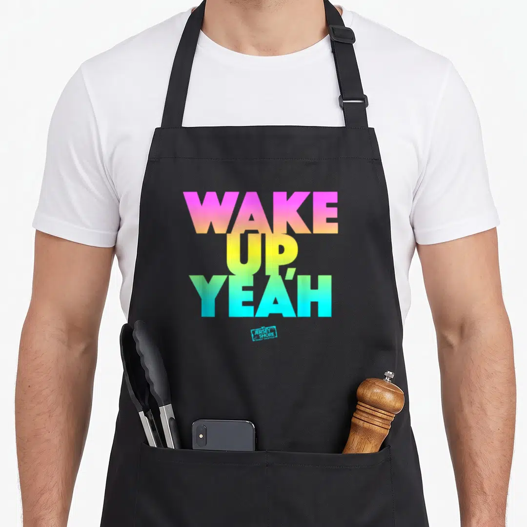 Jersey shore hawks apron - WAKE UP YEAH text in pink yellow green blue gradients with small logo below — shown on a black cotton canvas apron against a white background