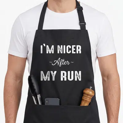 Jogging runner apron - White stacked typography reading I'M NICER ~After~ MY RUN on grey background — shown on a black cotton canvas apron against a white background