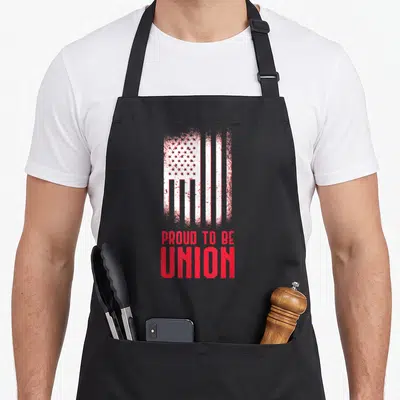 Skilled union aprons - Distressed vertical USA flag above red Proud To Be Union text — shown on a black cotton canvas apron against a white background