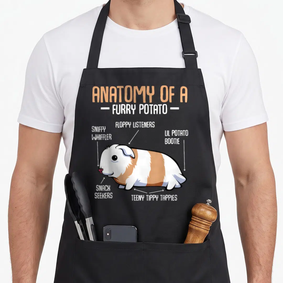 Anatomy household aprons - Cartoon guinea pig diagram with labels like floppy listeners and lil potato bootie in tan — shown on a black cotton canvas apron against a white background