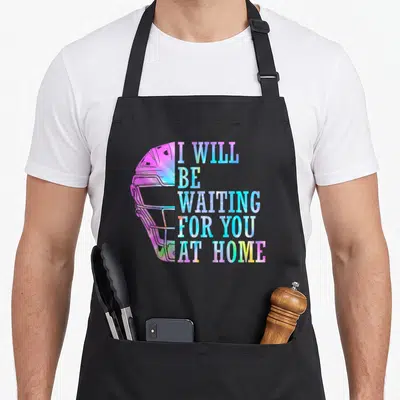 Waiting at home aprons - Tie-dye football helmet with stacked text I WILL BE WAITING FOR YOU AT HOME in pink blue — shown on a black cotton canvas apron against a white background