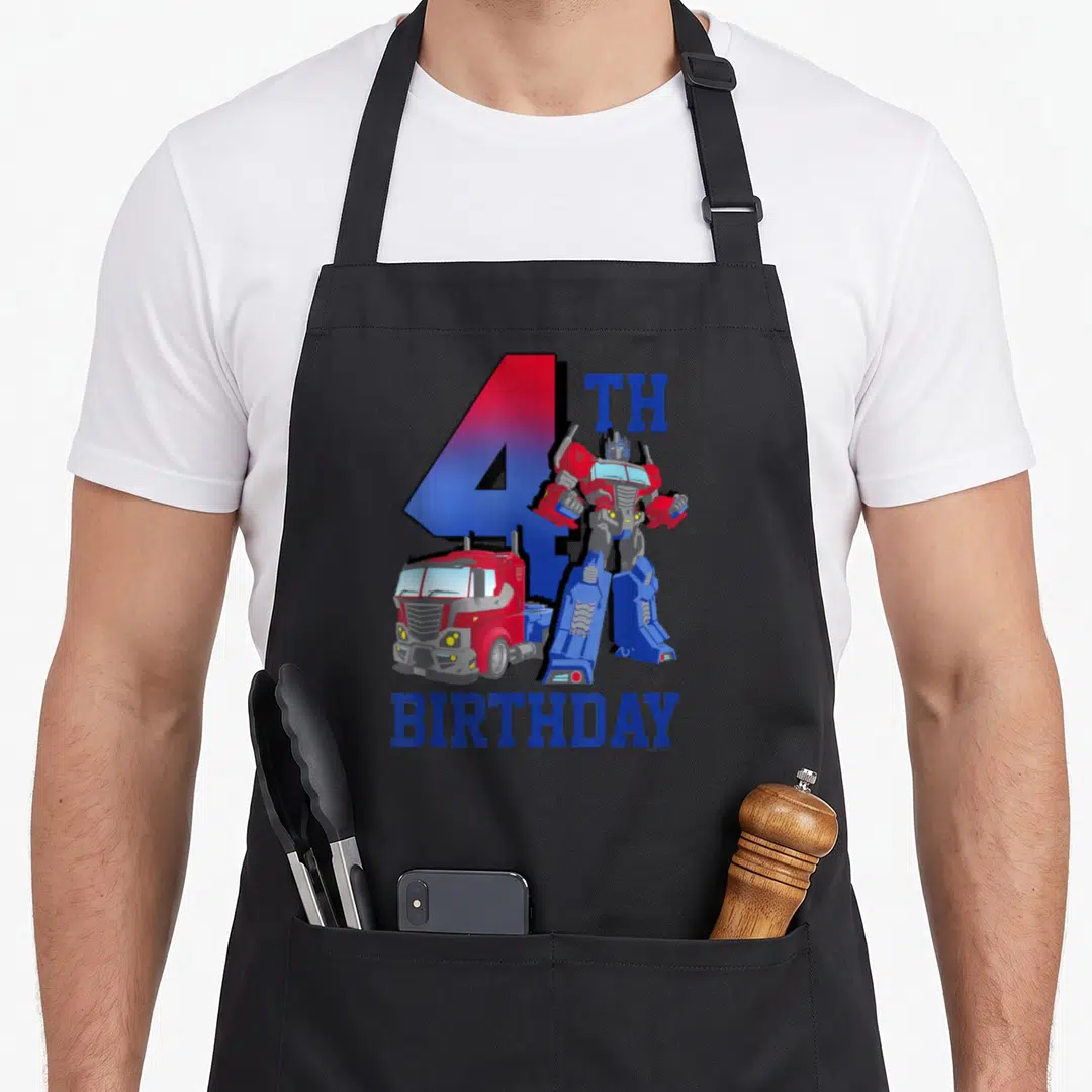 Fill birthday apron - Optimus Prime robot and red truck beside large blue number 4 with BIRTHDAY text — shown on a black cotton canvas apron against a white background