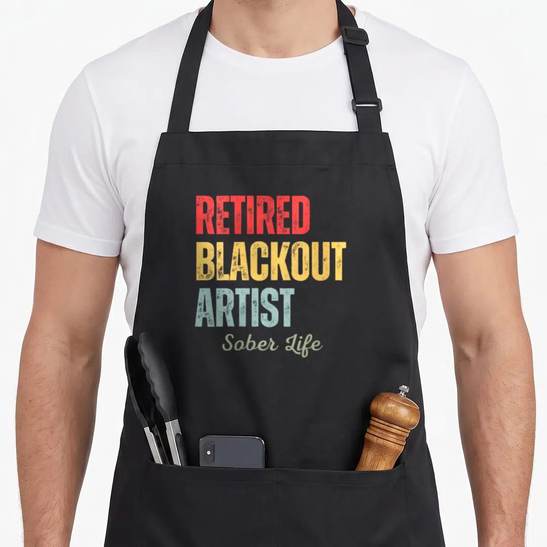 Retired alcohol recovery apron - Stacked text reading Retired Blackout Artist Sober Life in red yellow blue and green — shown on a black cotton canvas apron against a white background
