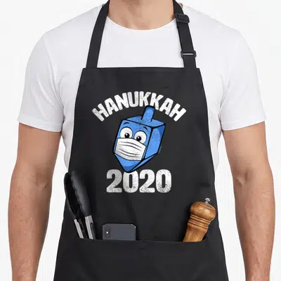 Dreidel hanukkah apron - Blue dreidel in white mask with HANUKKAH 2020 text in cartoon style — shown on a black cotton canvas apron against a white background