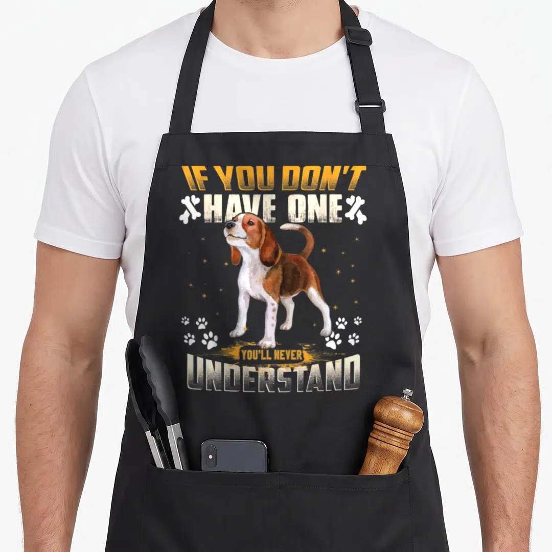 Youll dog apron - Beagle standing between orange and white text flanked by bones and scattered paw prints — shown on a black cotton canvas apron against a white background
