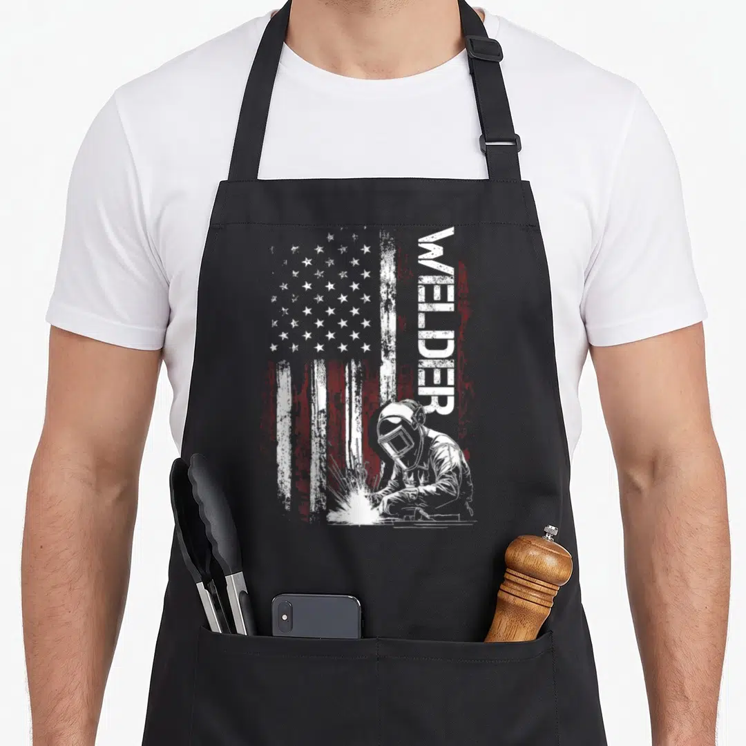 Welder welding american flag apron - Vertical WELDER text next to a distressed white and red USA flag with a welding — shown on a black cotton canvas apron against a white background