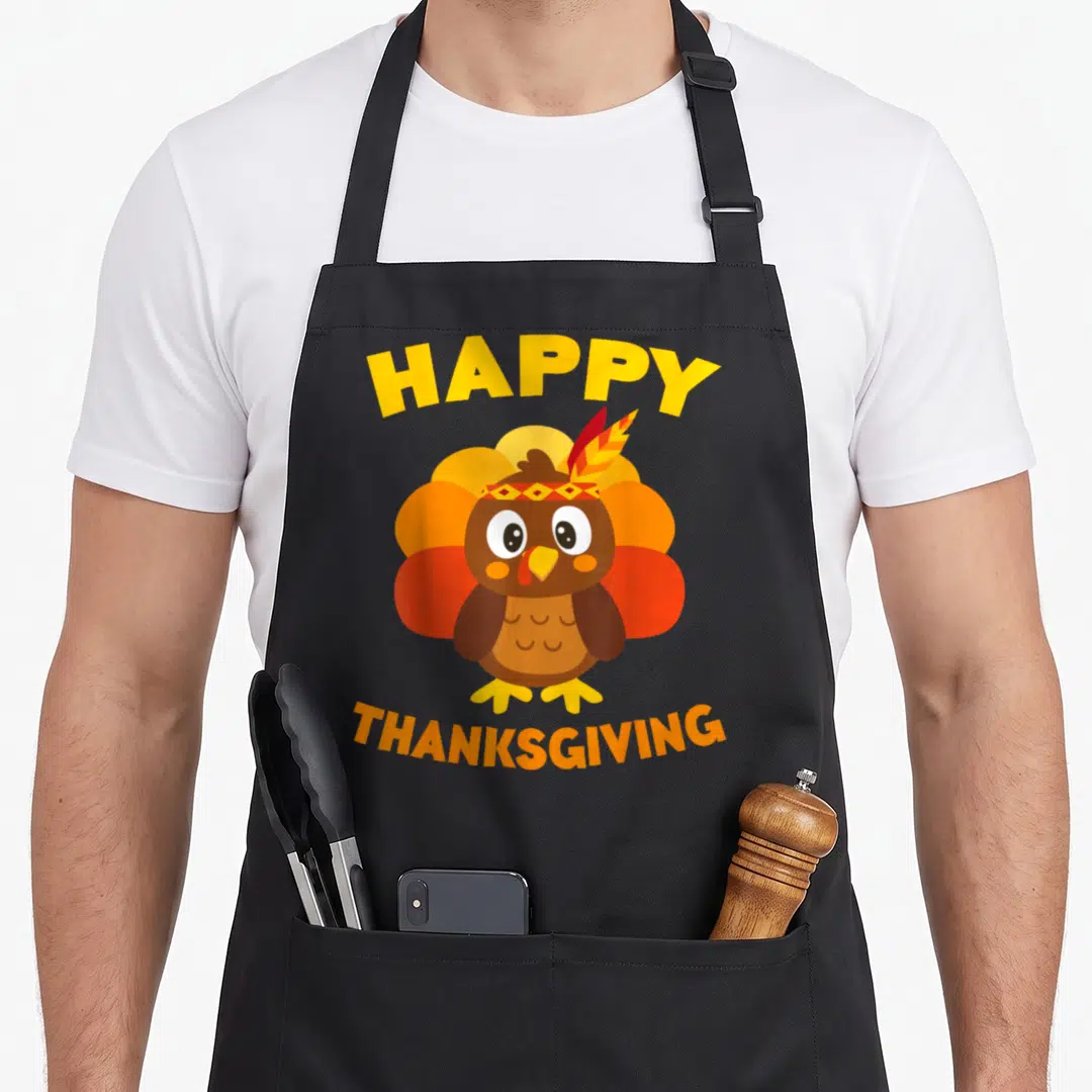 Family turkey thanksgiving day aprons - Cartoon brown turkey with red and orange feathers wearing a patterned headband — shown on a black cotton canvas apron against a white background