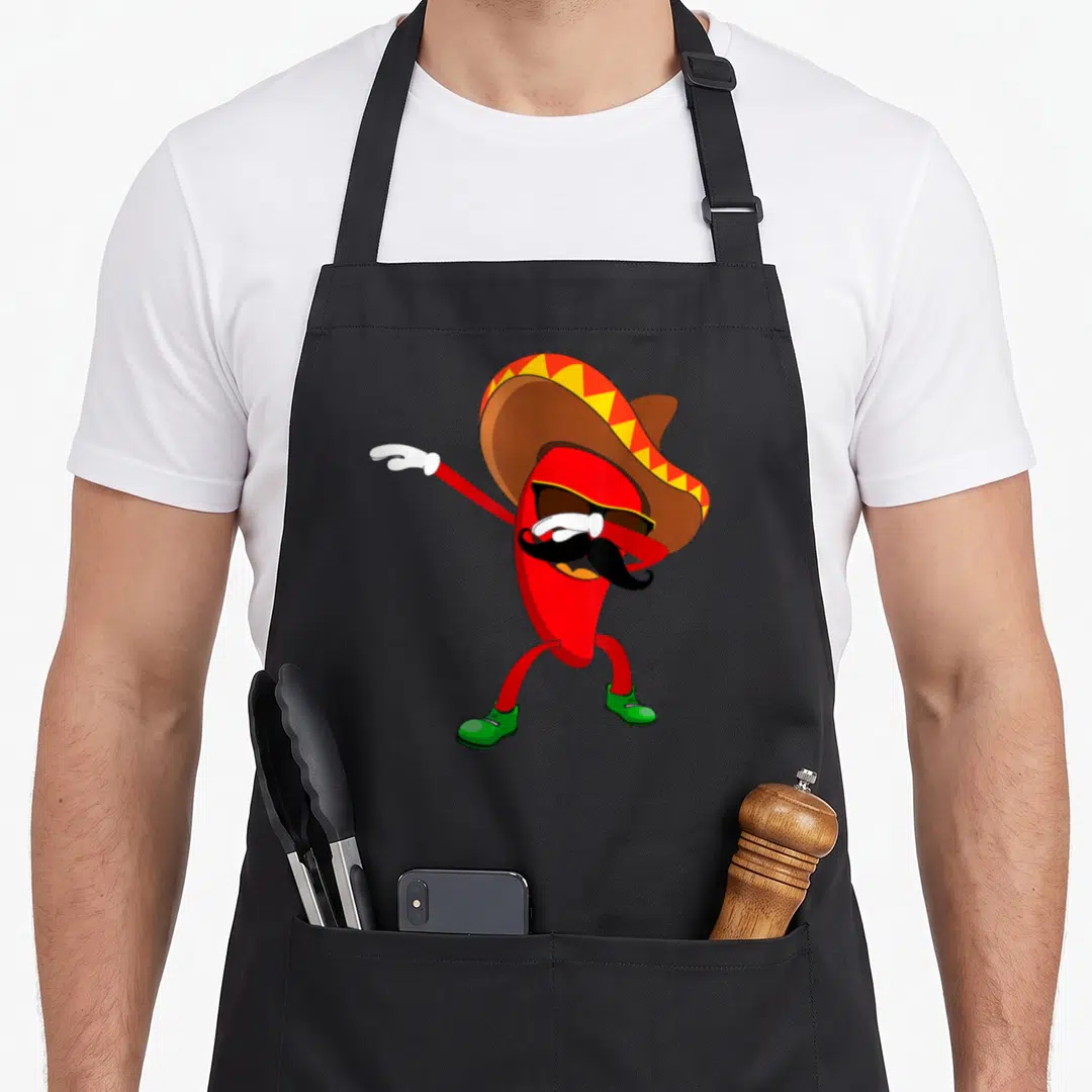Dabbing chili pepper apron - Red cartoon chili wearing brown sombrero yellow trim green shoes black mustache sunglasses — shown on a black cotton canvas apron against a white background